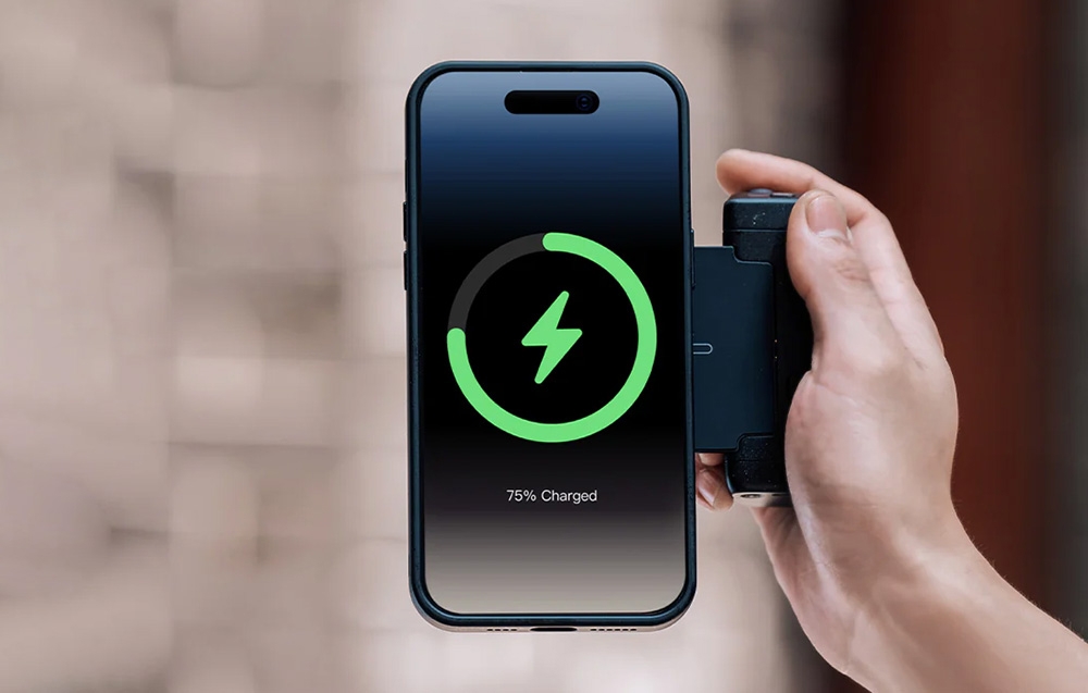 Kéz tart egy telefont, amelynek képernyője 75%-os akkumulátor töltöttséget mutat, mellette csatlakoztatott fekete powerbank kábellel