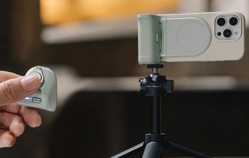 iPhone in a light green case with a grip mounted on a tripod, next to a hand holding the remote control