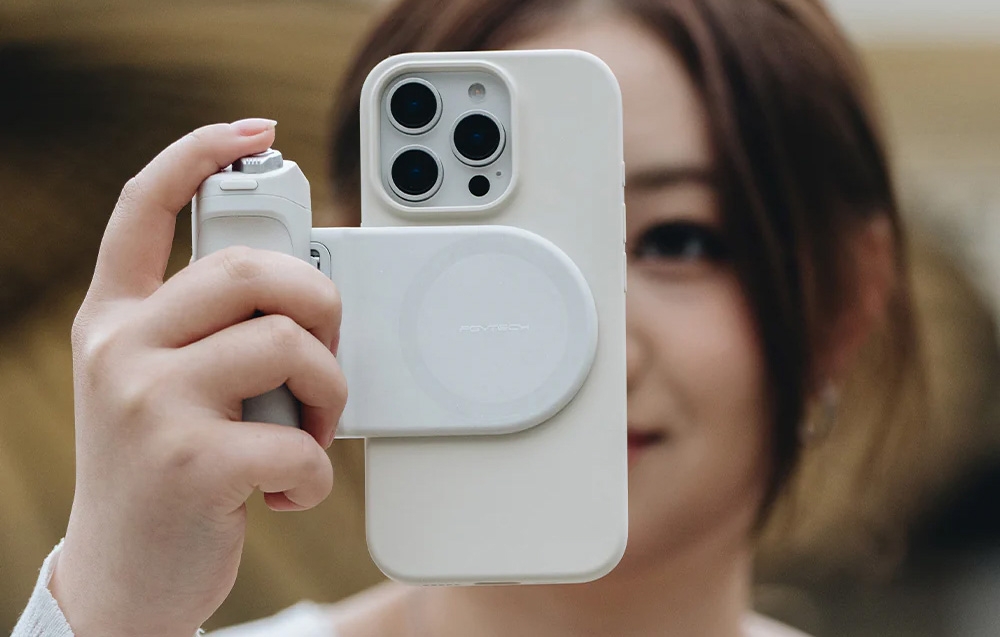 Woman holding an iPhone in a white case with a MagSafe power bank and wrist strap, camera facing forward