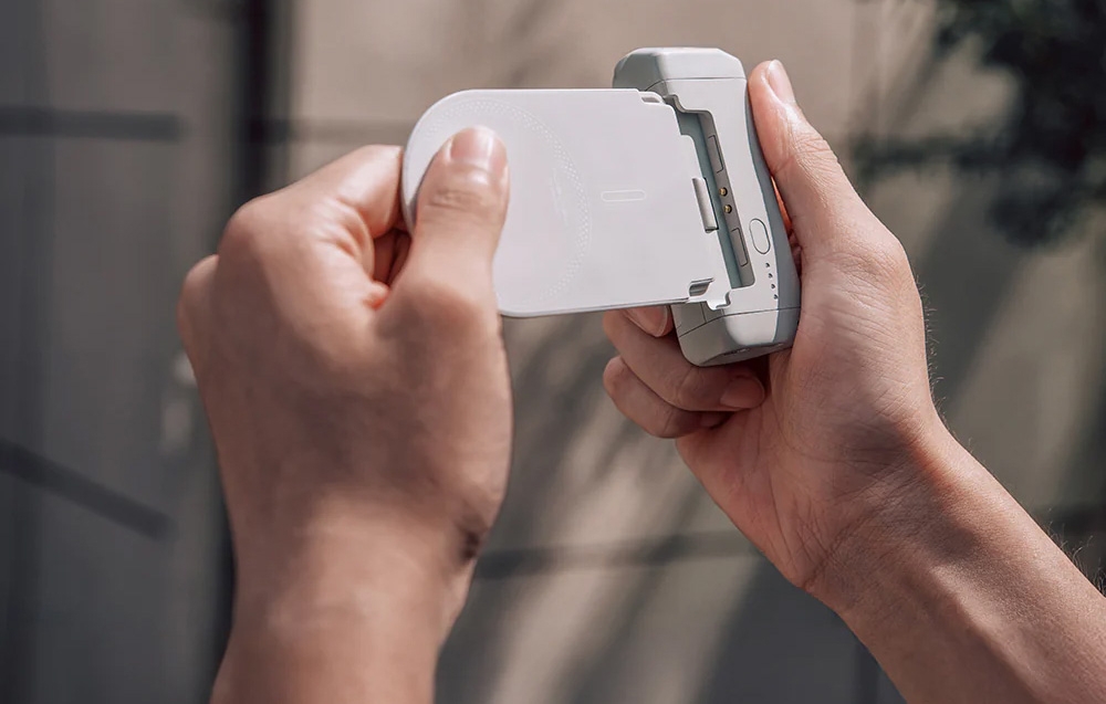 Two hands attaching a white magnetic power bank to the back of a silver iPhone, side view of the device