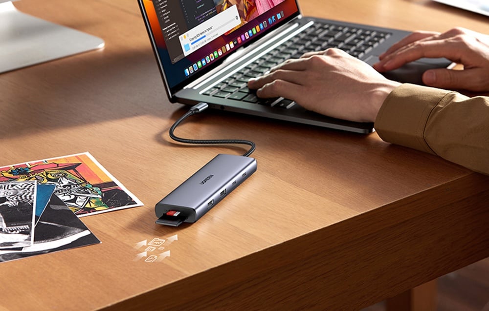 Hub UGREEN z podłączoną kartą SD leżący obok laptopa, przy którym pracuje użytkownik.