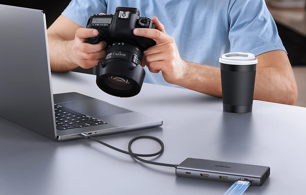 Mężczyzna trzymający aparat fotograficzny przy laptopie z podłączonym hubem UGREEN i kartą SD.