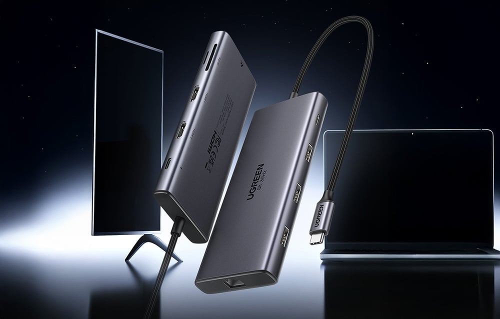 Dwa unoszące się huby UGREEN z widocznymi portami na tle monitora i laptopa w ciemnym otoczeniu.