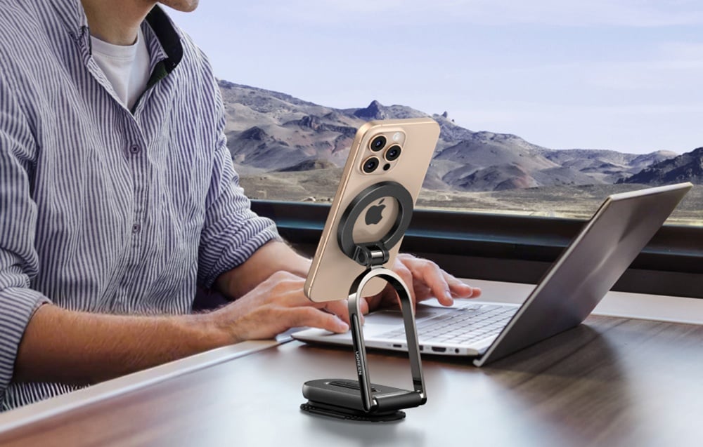 iphone w uchwycie magnetycznym stoi obok laptopa, na którym pracuje mężczyzna w pociągu