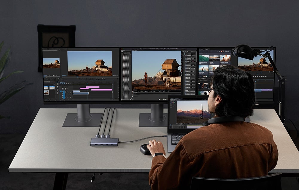 Mężczyzna edytujący wideo na laptopie i trzech monitorach podłączonych przez hub UGREEN.