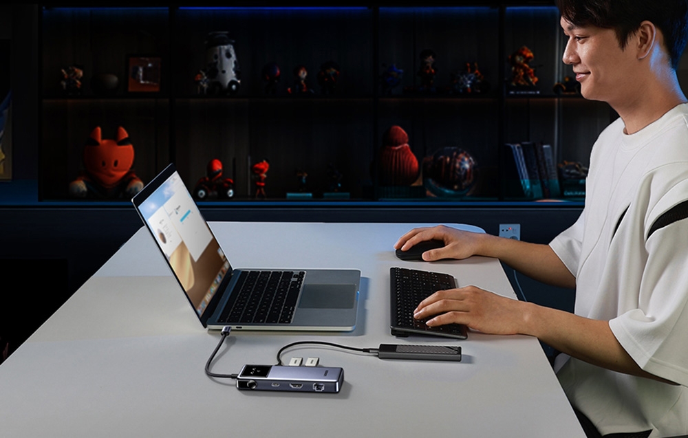  Mężczyzna przy biurku pracujący na laptopie podłączonym do hubu UGREEN z wyświetlaczem i akcesoriami.