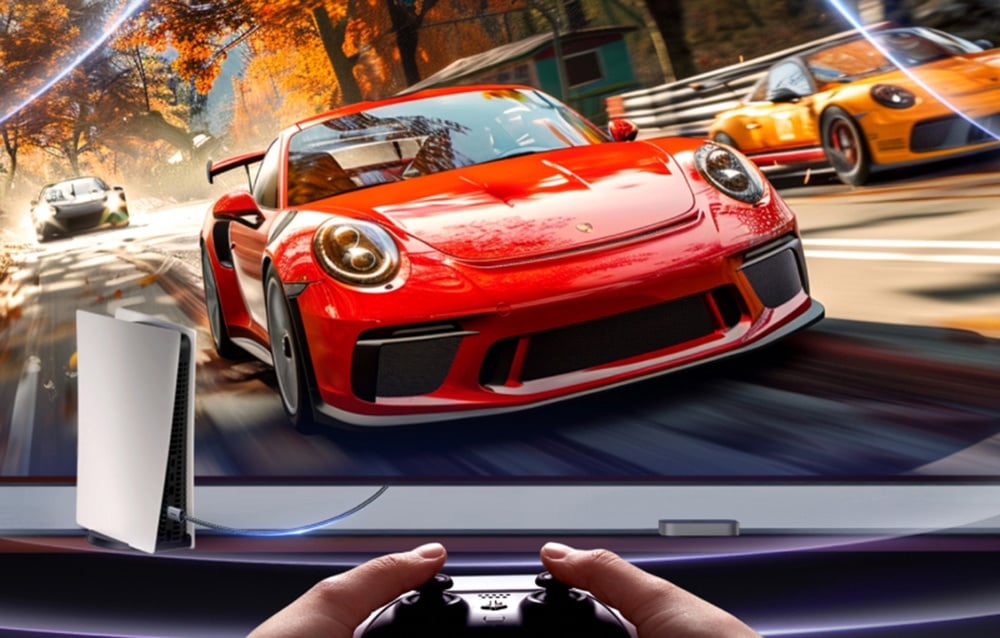 Duży ekran, na którym wyświetla się czerwony samochód; widać dłonie osoby trzymającej kontroler.