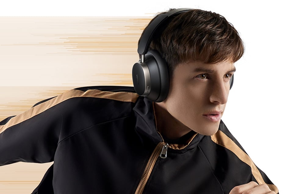 mężczyzna w sportowej bluzie patrzy przed siebie słuchając muzyki na czarnych nausznych słuchawkach