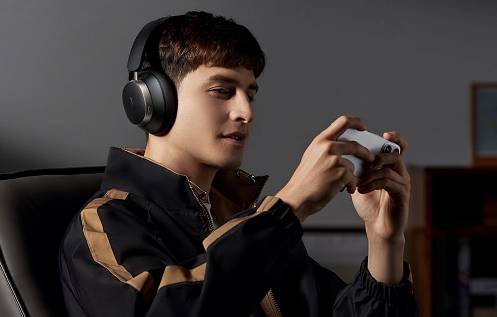 mężczyzna w bluzie gra na telefonie mając na głowie słuchawki