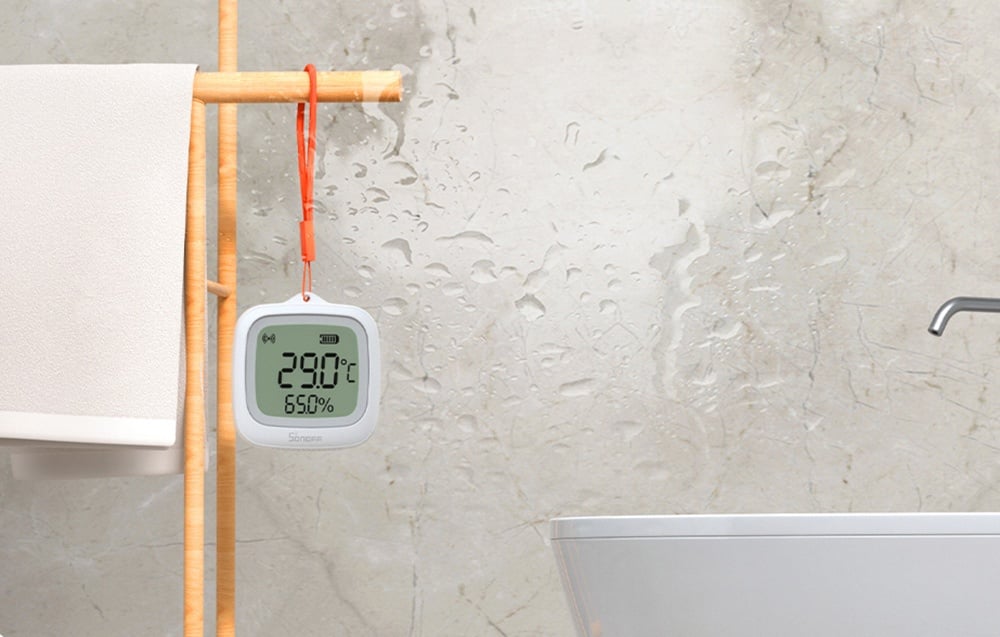 sensor hanging in a bathroom next to a towel showing a temperature of 29 degrees Celsius and 65% humidity