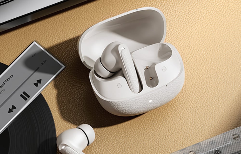 Białe słuchawki bezprzewodowe w otwartym etui leżące na stole obok winyla i odtwarzacza muzyki.