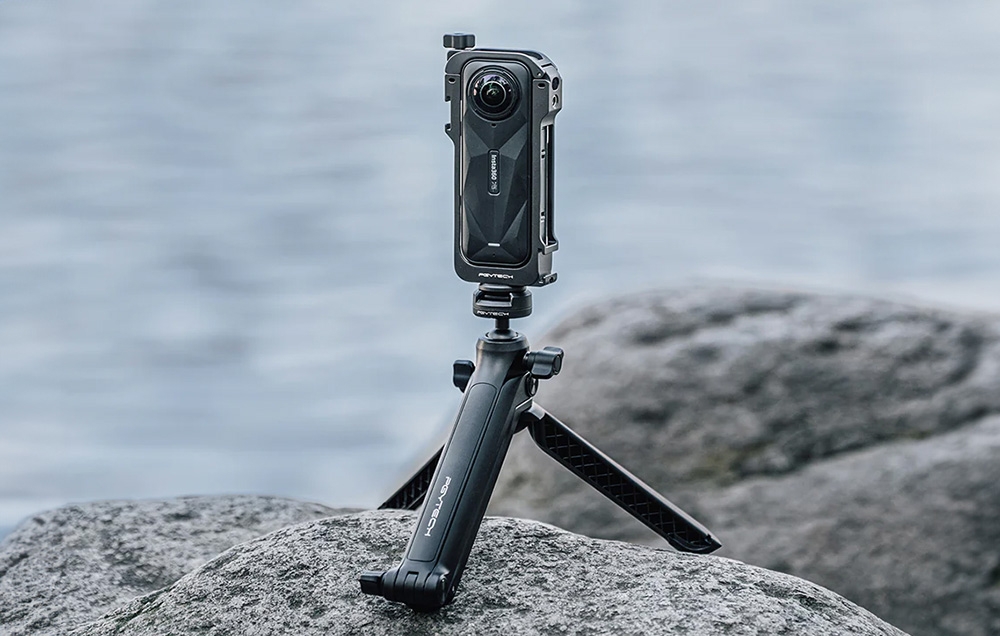 Kamera insta360 X5 w obudowie i na statywie leży na kamieniu. W tle widać wodę.