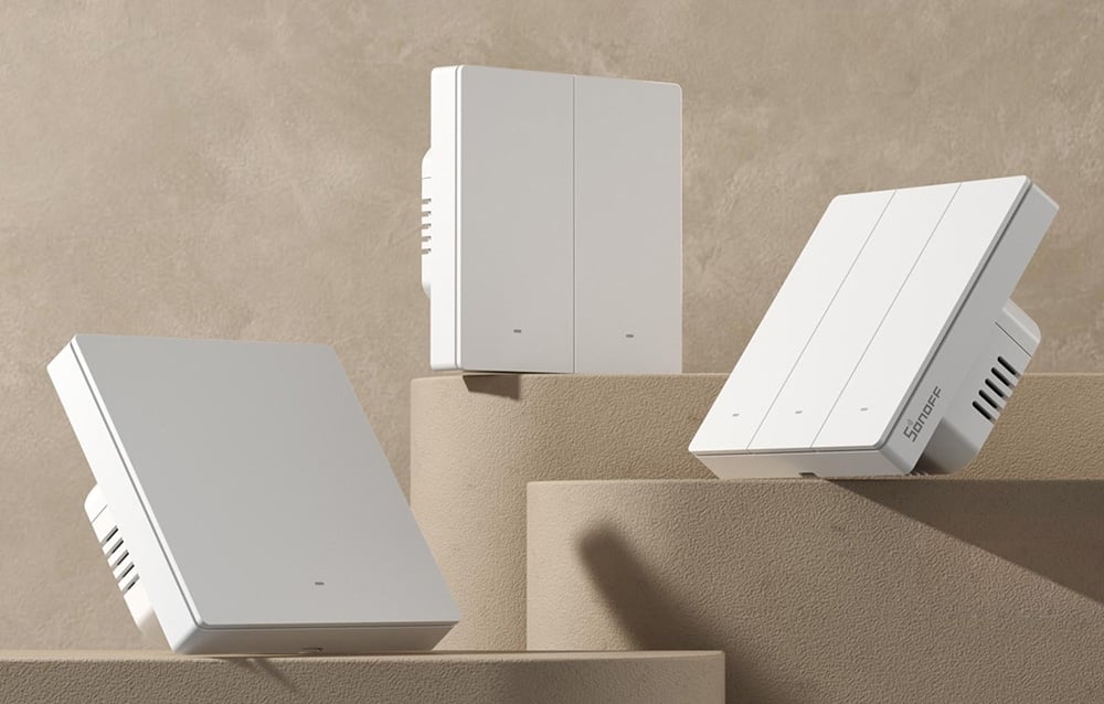 Trzy białe inteligentne przełączniki SONOFF różnych typów ułożone na beżowych geometrycznych blokach