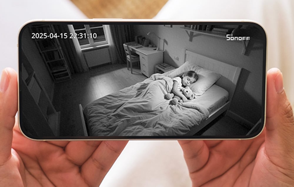 Dłonie trzymające smartfon z aplikacją SONOFF pokazującą dziecko śpiące w łóżku w noktowizji