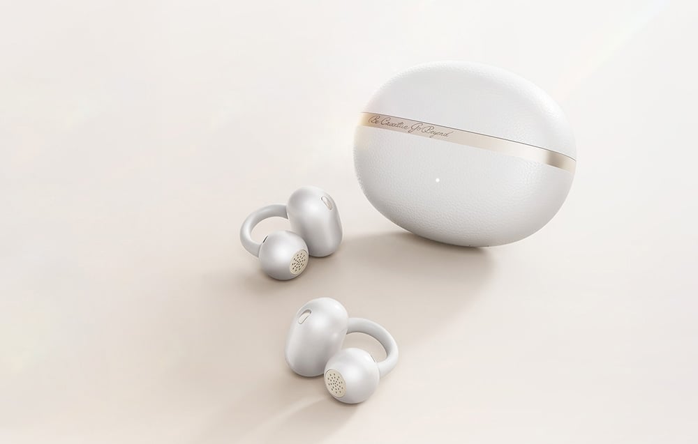 Para białych słuchawek bezprzewodowych leżąca obok zamkniętego, białego etui z napisem