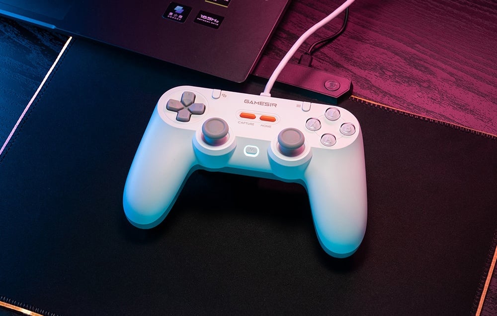 Biały przewodowy kontroler GameSir podłączony do laptopa i leżący na podkładce.