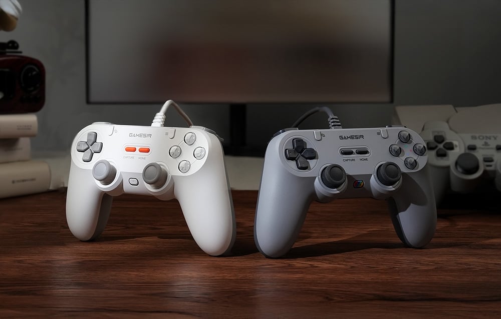 Dwa przewodowe kontrolery GameSir, biały i szary, ustawione obok siebie na drewnianym blacie.