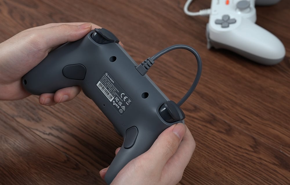 Widok z tyłu na trzymany w dłoniach szary kontroler GameSir z podłączonym przewodem.