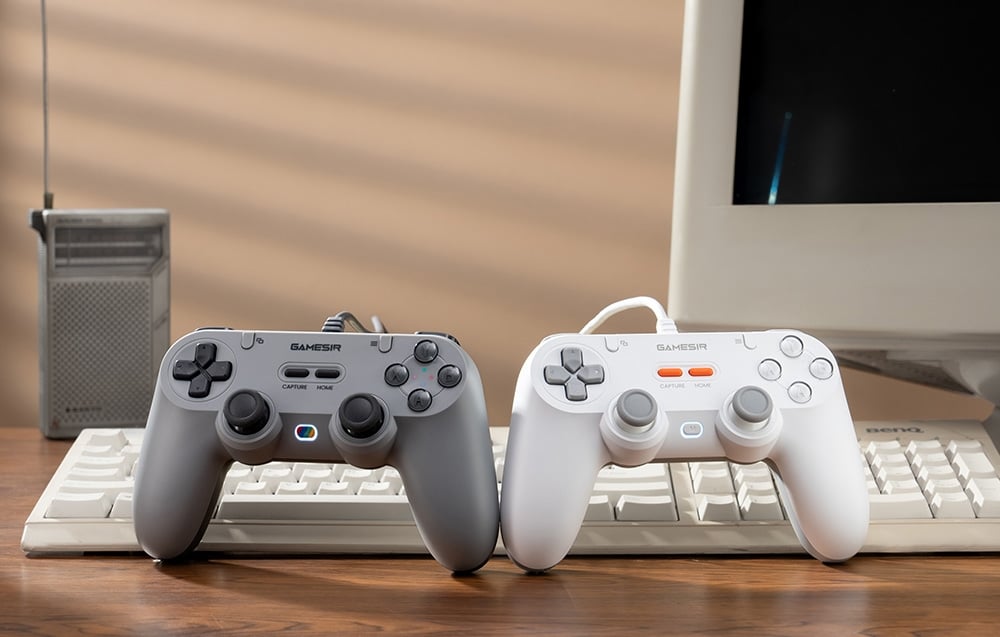 Szary i biały kontroler GameSir ustawione na klawiaturze przed monitorem i radiem.