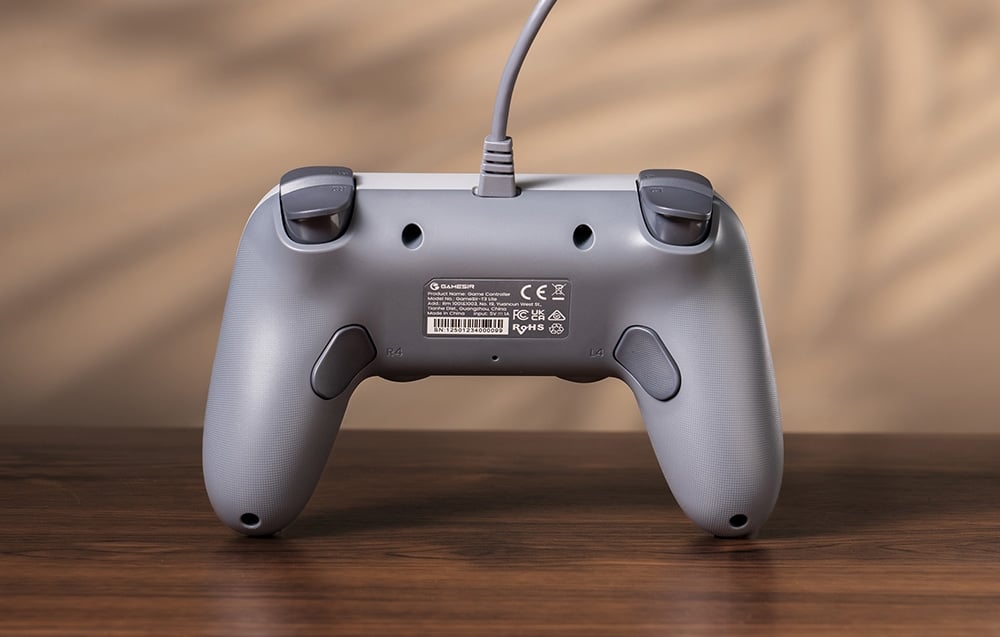 Tył szarego kontrolera GameSir z widocznymi przyciskami, etykietą i przewodem na tle drewnianego stołu.