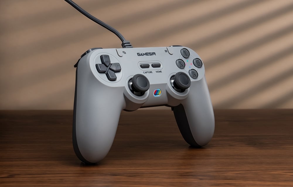 Szary kontroler GameSir stojący pionowo na drewnianym blacie z widocznymi przyciskami i podświetleniem.