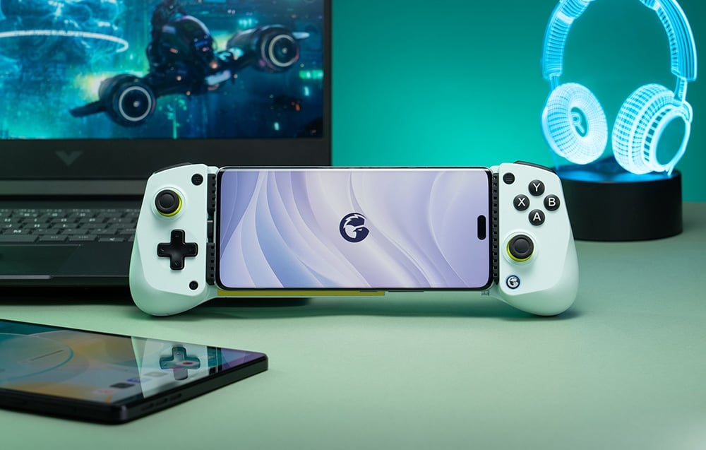 Smartfon zamocowany w białym kontrolerze GameSir ustawionym przed laptopem i lampką w kształcie słuchawek.