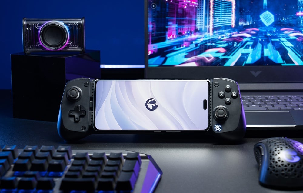  Smartfon zamontowany w czarnym kontrolerze GameSir ustawionym na biurku przed laptopem i akcesoriami gamingowymi.