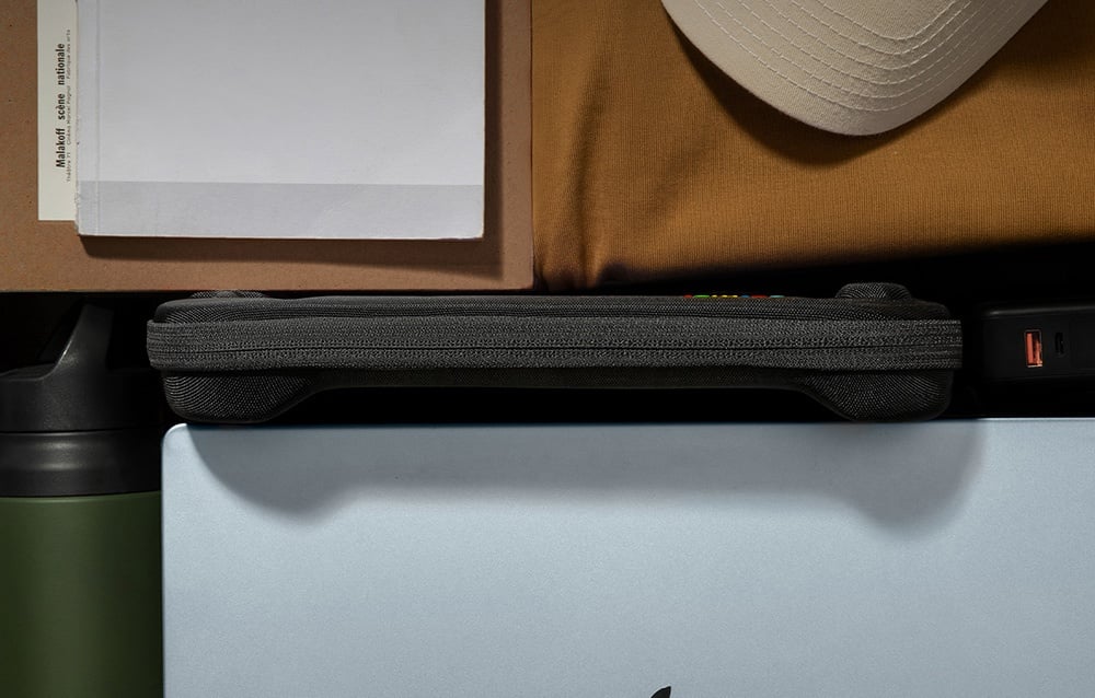 Zamknięte czarne etui z kolorowym logo tomtoc w obok czapki i dokumentów