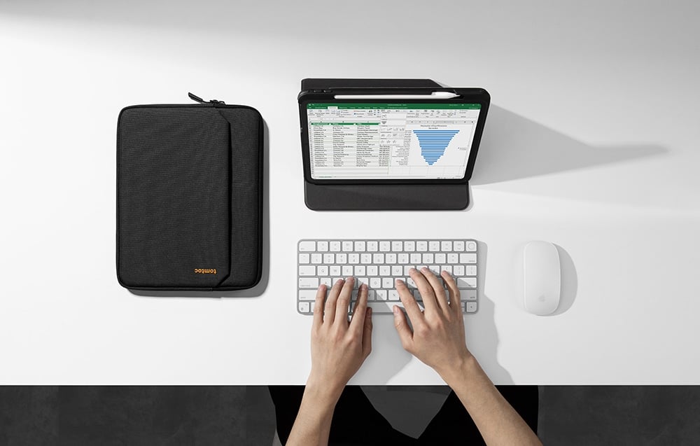ęce na klawiaturze przy iPadzie z wykresem Excel obok czarnego etui tomtoc