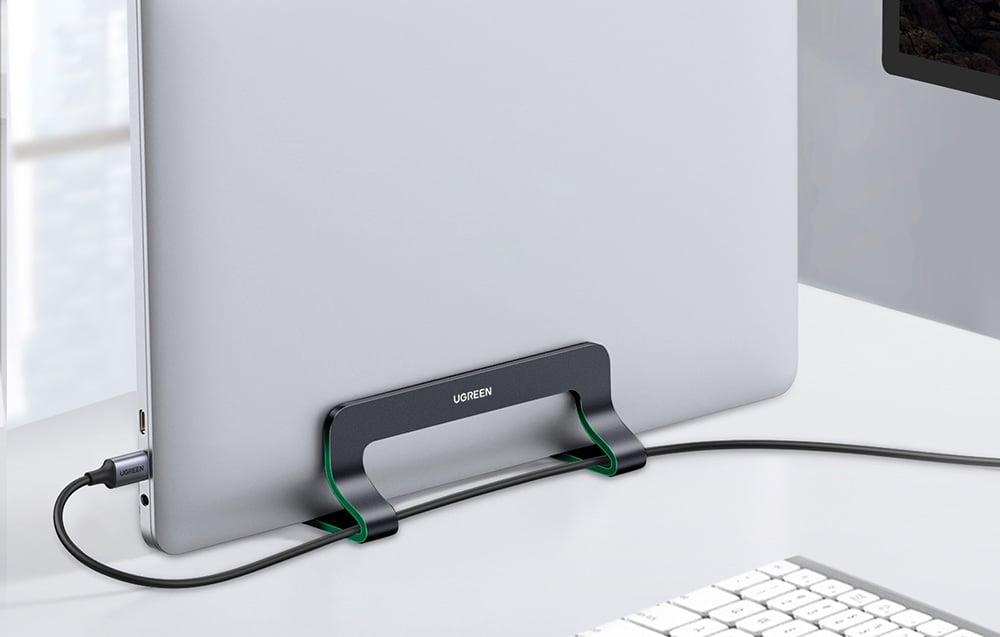 A MacBook in a UGREEN stand with cables connected on a white desk