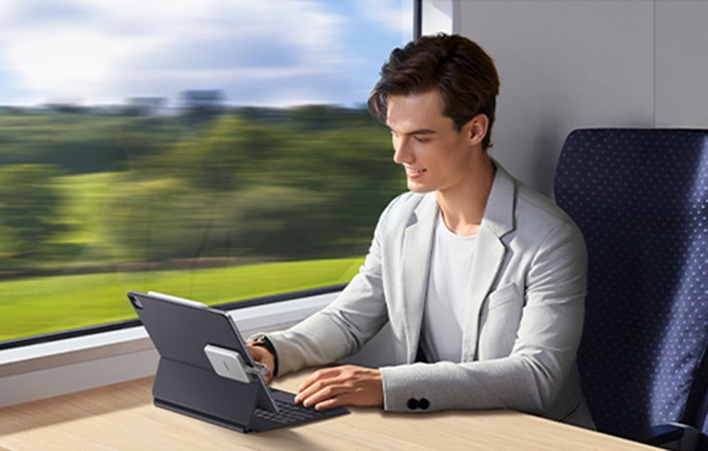 A man in a gray suit using a laptop on a train by the window with a view of the landscape