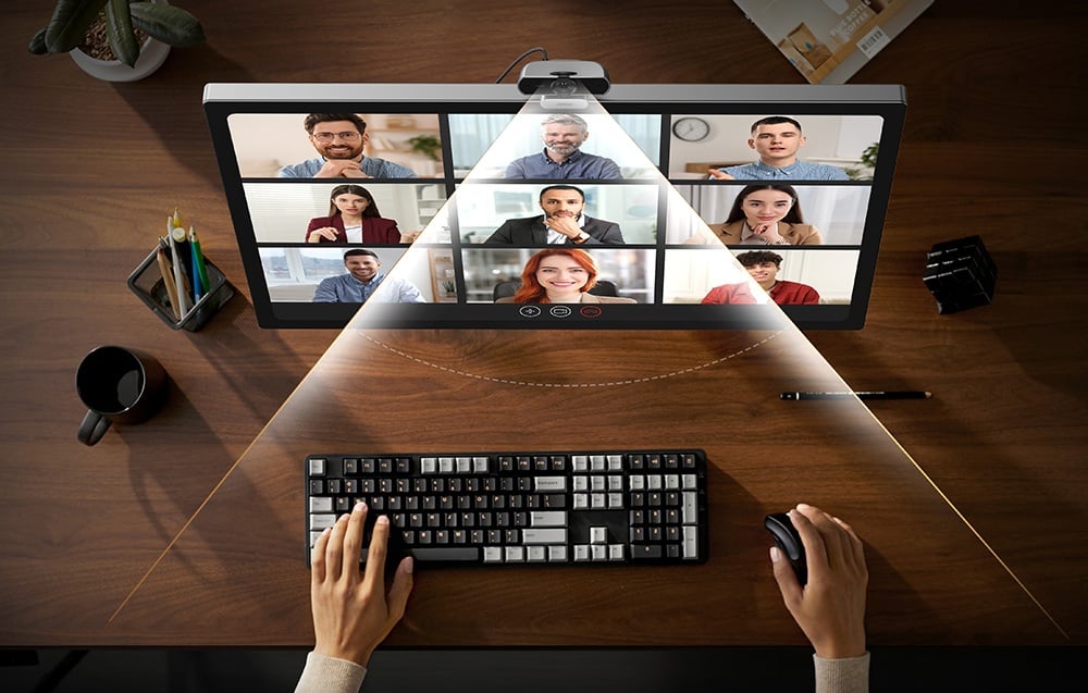 Bird's eye view of a video conference - hands on the keyboard, monitor with nine participants and webcam