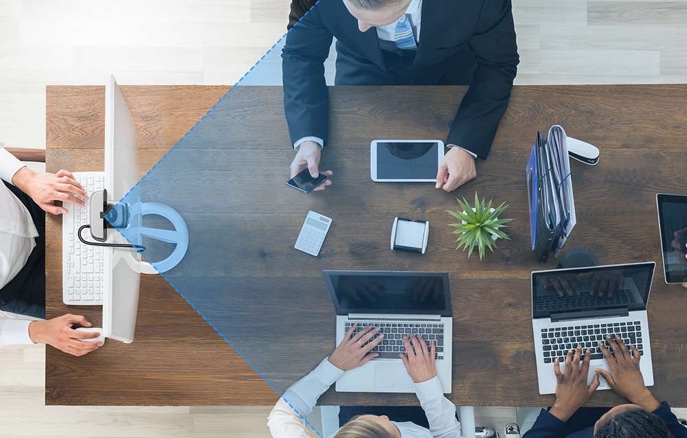 Bird's-eye view of a business meeting at a wooden table with laptops, tablets, and participants