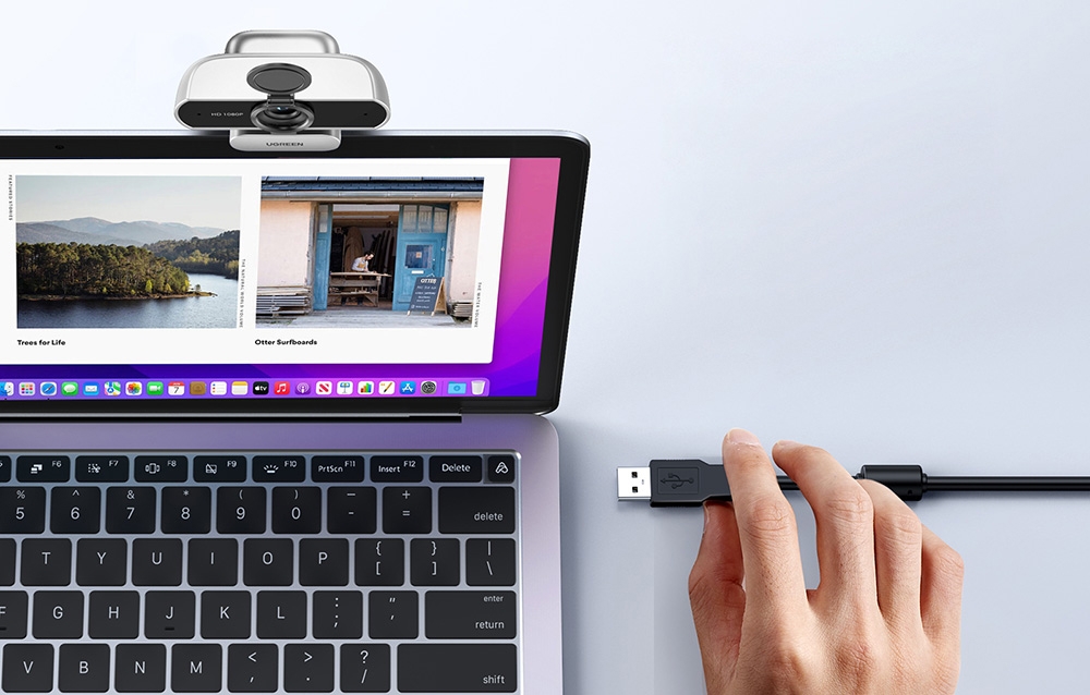 Hand connecting USB cable to a laptop with a webcam and colorful images on the screen