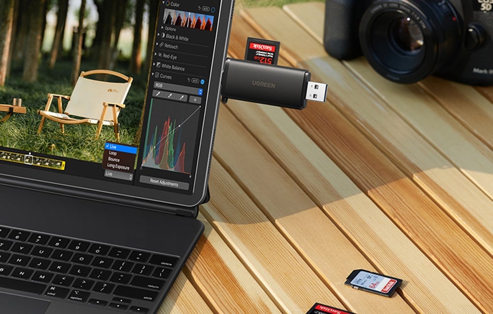 memory card reader with an inserted card connected to a laptop with photo editing software on a wooden surface, next to a camera