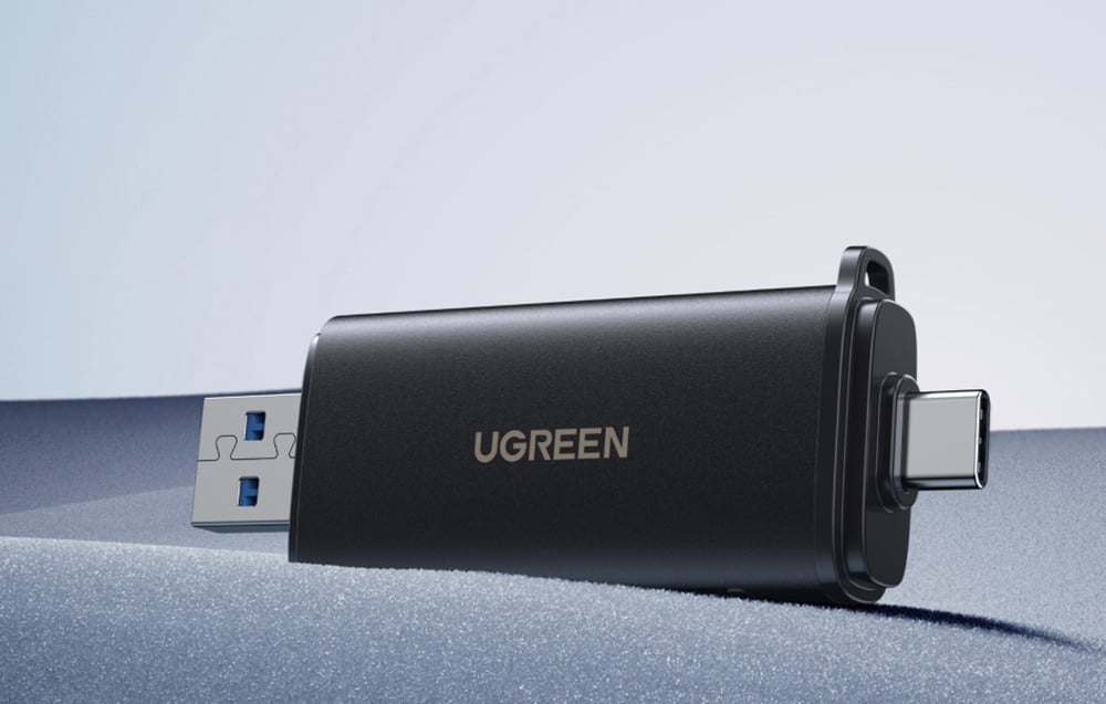 Black UGREEN adapter with USB-A and USB-C plugs lying on a gray surface on a minimalist background