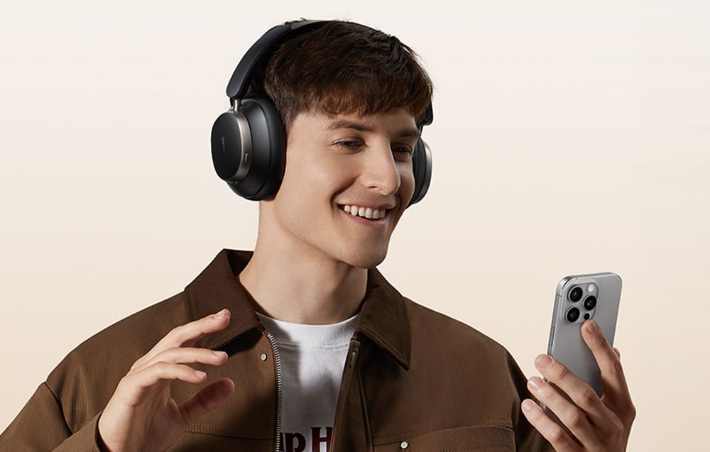 Chłopak z czarnymi słuchawkami na głowie uśmiecha się do telefonu