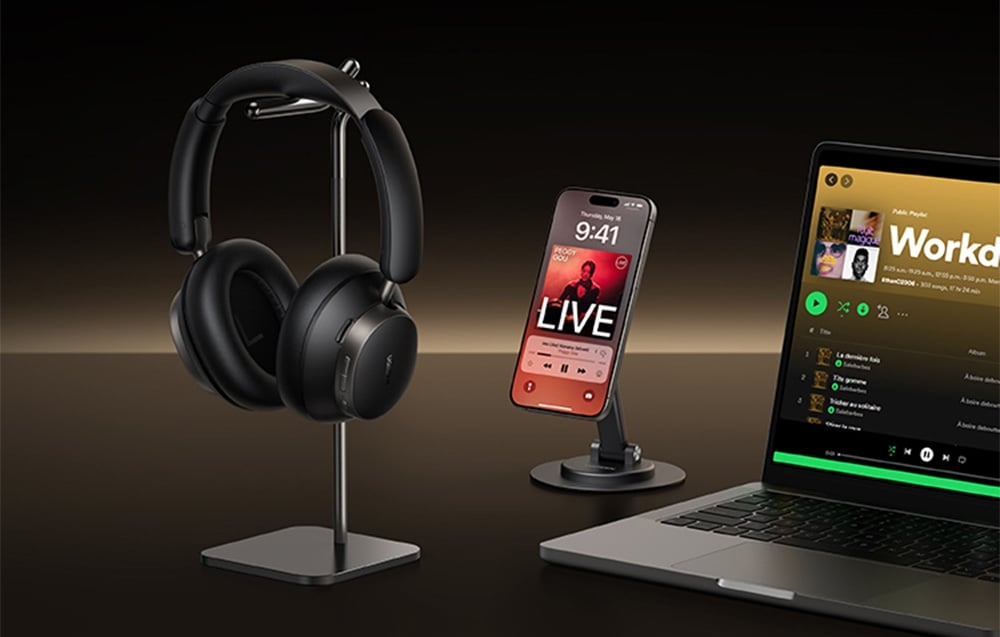 Czarne słuchawki nauszne na stojaku, smartfon i otwarty laptop na ciemnym tle