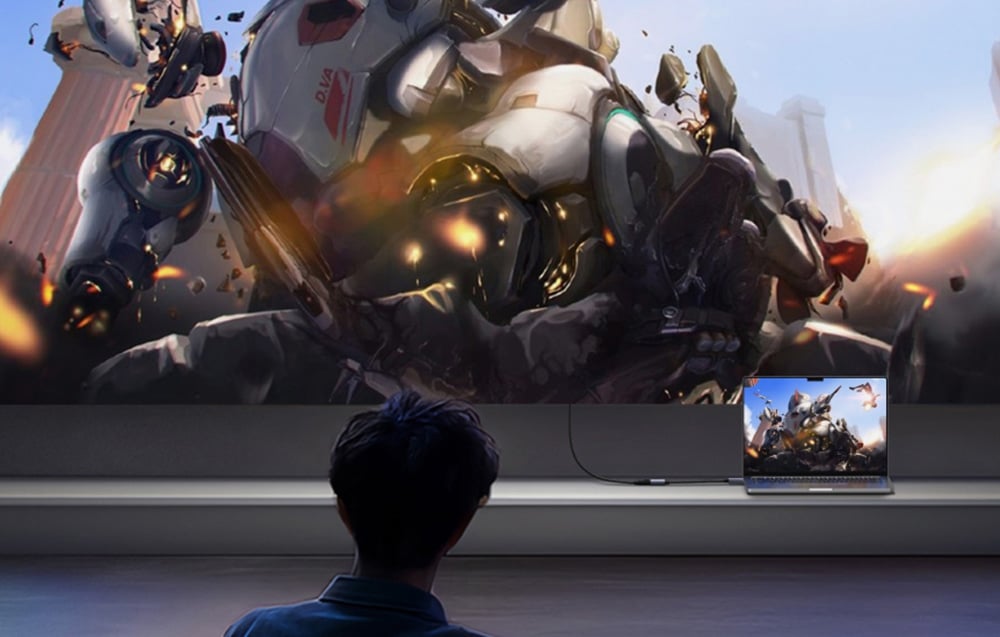 Osoba ogląda grę z robotami wyświetlaną na dużym ekranie z laptopa połączonego kablem