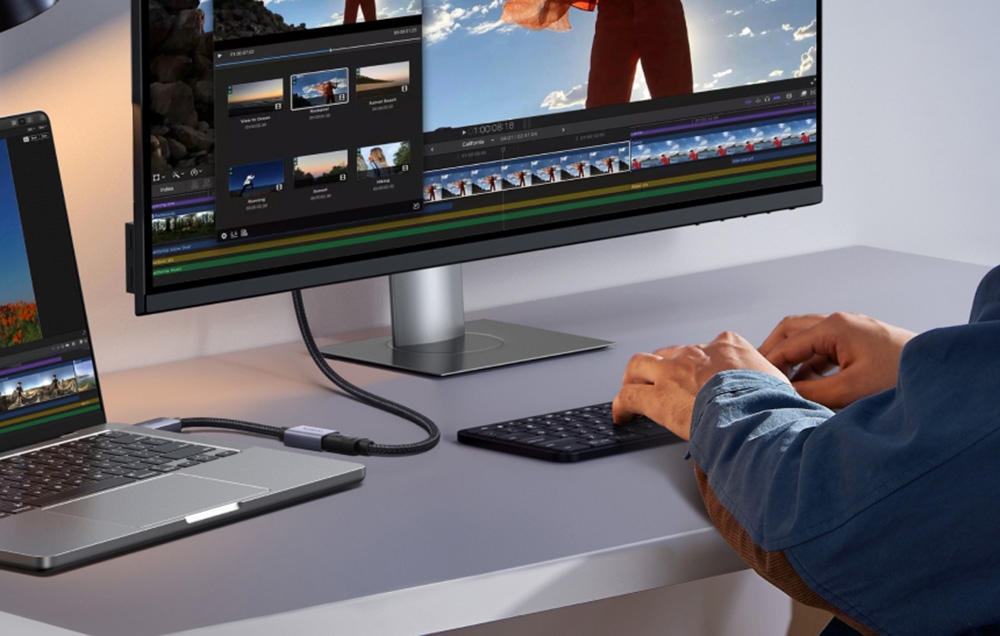 Stanowisko pracy z monitorem i laptopem połączonymi kablem, osoba pracuje nad edycją wideo
