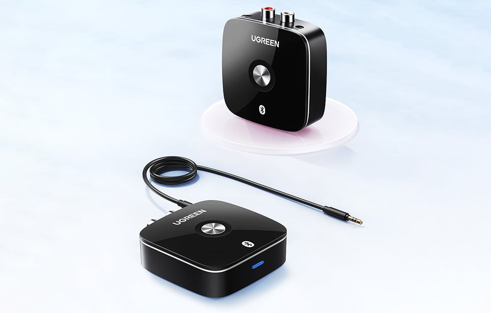 Dwa czarne adaptery Bluetooth UGREEN z kablem audio, jeden na przezroczystej podstawce