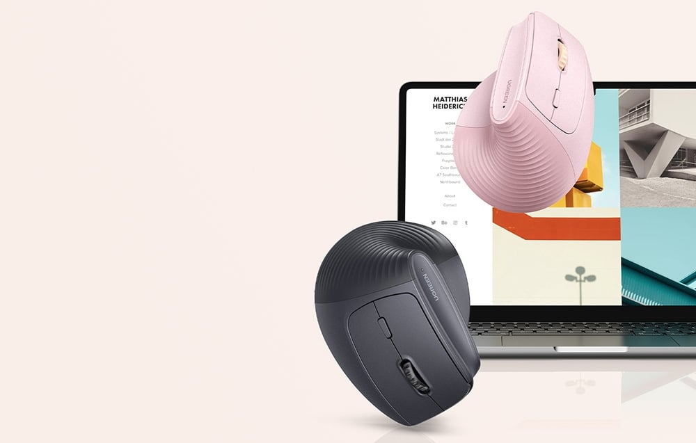 Różowa i czarna myszka UGREEN unoszące się nad ekranem laptopa z grafiką architektoniczną