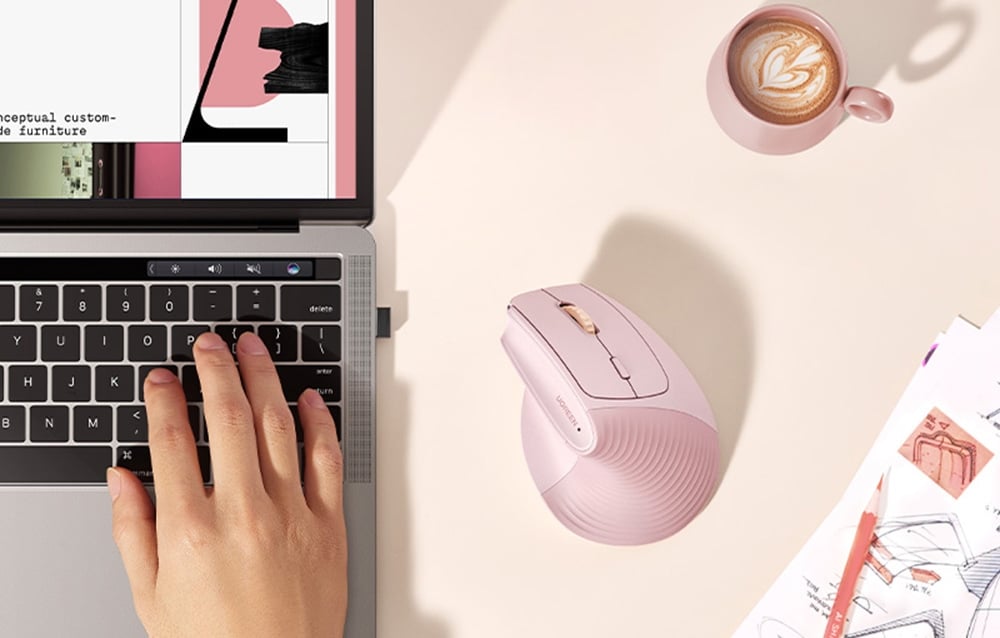 Różowa myszka UGREEN obok laptopa, filiżanki kawy i szkiców na jasnym biurku