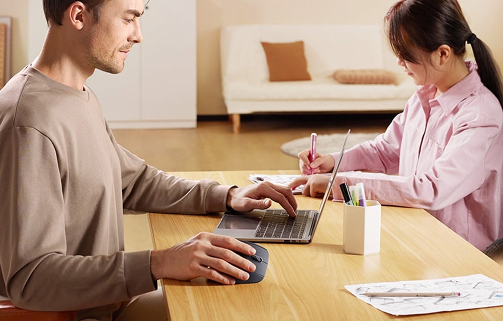 Mężczyzna korzystający z laptopa i myszki UGREEN podczas pracy przy stole z towarzyszącą osobą