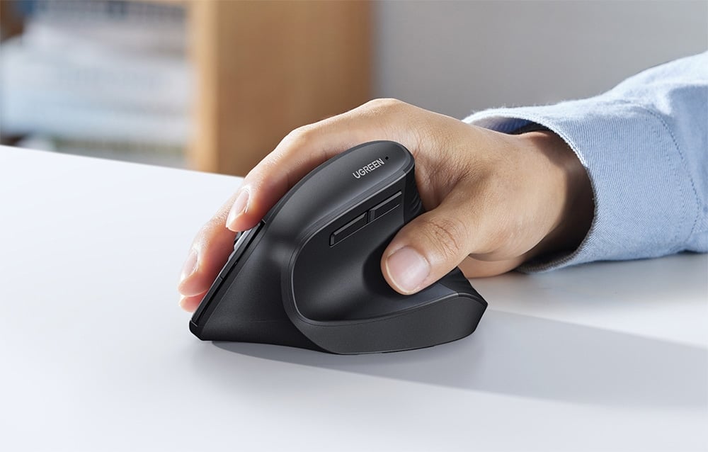 Dłoń trzymająca pionową ergonomiczną myszkę UGREEN podczas pracy przy biurku