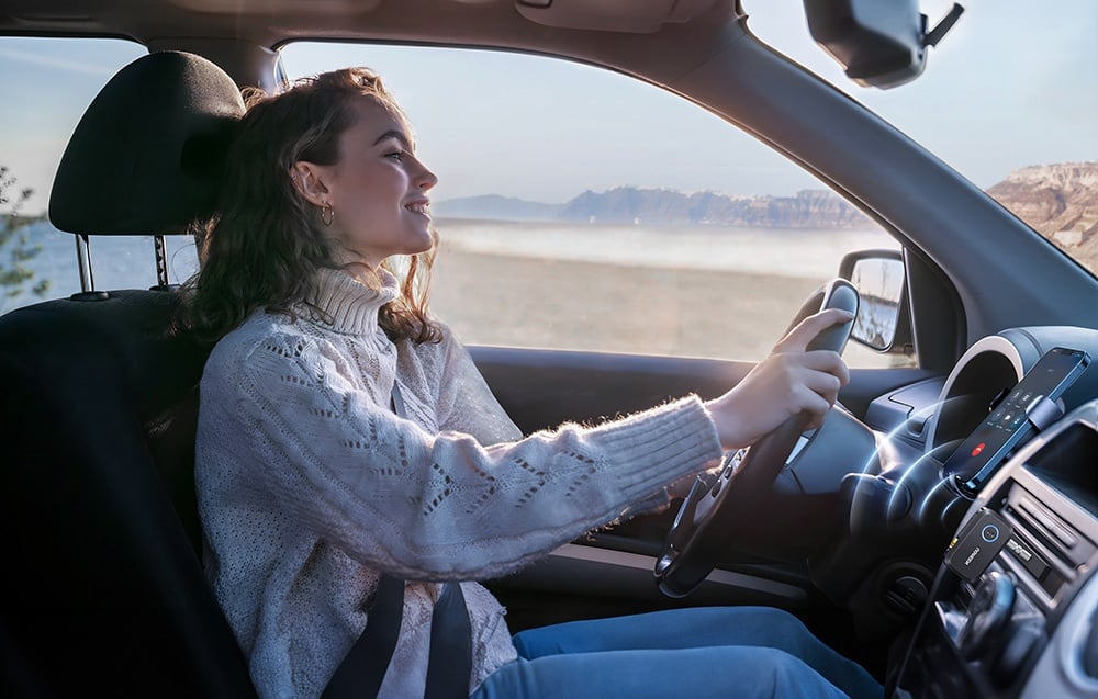 Kobieta w białym swetrze prowadzi samochód na tle górskiego krajobrazu