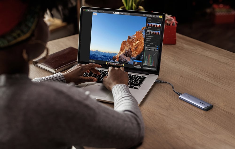 A woman working on a laptop with photo editing software and a connected UGREEN SSD