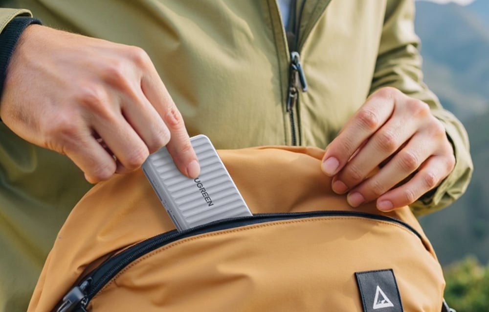 Person steckt den grauen Kartenleser der Marke UGREEN in die vordere Tasche eines Rucksacks