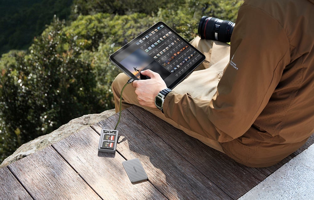 Mann sitzt am Rande einer Terrasse in den Bergen und durchsucht Fotos auf einem Tablet, das an den Kartenleser angeschlossen ist