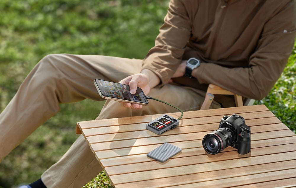 Mann durchsucht Fotos auf einem Smartphone, das an den Kartenleser angeschlossen ist, der neben der Kamera liegt